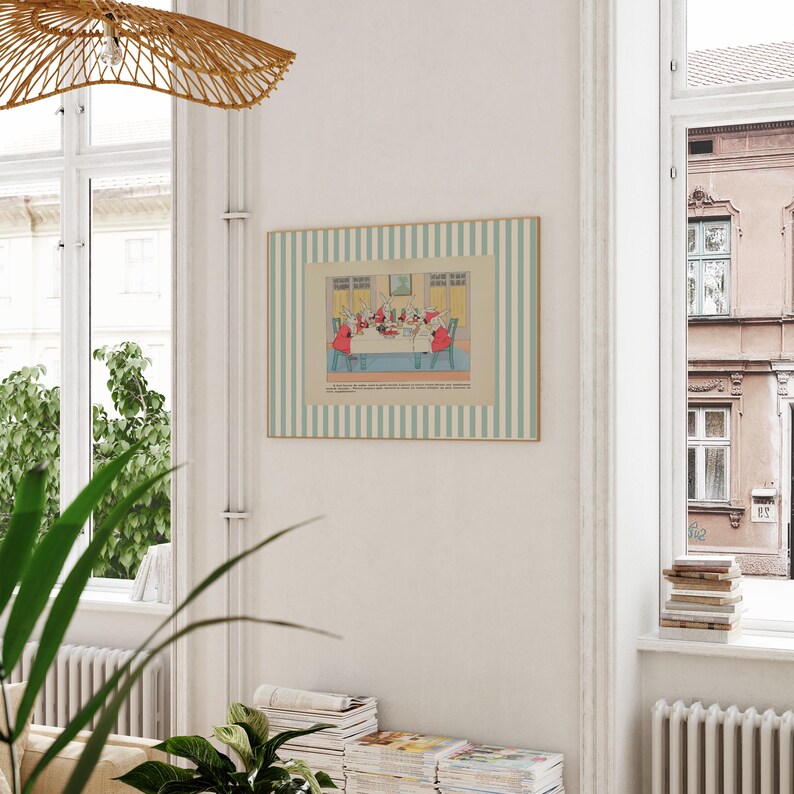 May include: A framed vintage print with a light blue and white striped border. The print depicts a gathering of figures around a table, with red and white details. The artwork is displayed on a white wall in a room with natural light.