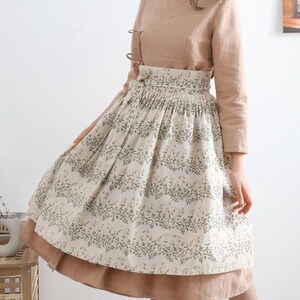 Puede incluir: Una falda beige y marr&oacute;n con estampado floral. La falda tiene una cintura plisada y un dobladillo fruncido. La falda se lleva con una blusa beige.