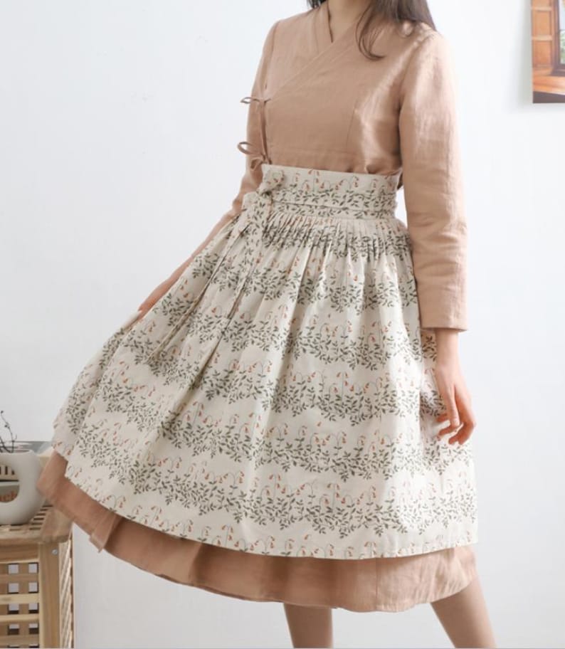 Puede incluir: Una falda beige y marr&oacute;n con estampado floral. La falda tiene una cintura plisada y un dobladillo fruncido. La falda se lleva con una blusa beige.
