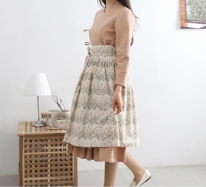 Puede incluir: Una falda beige y marr&oacute;n con estampado floral. La falda es plisada y tiene una cintura ancha. La falda se lleva con una blusa marr&oacute;n claro.