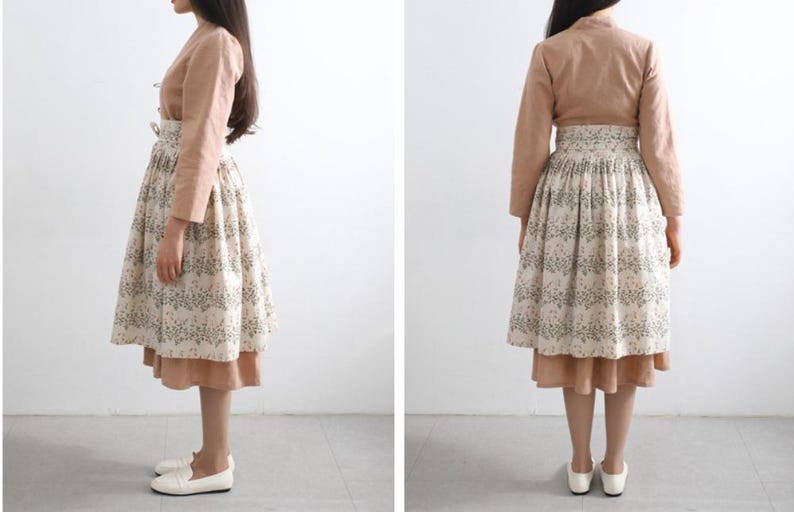 Puede incluir: Una blusa de manga larga de color marr&oacute;n claro con cuello alto y una falda blanca con estampado floral. La falda tiene una falda interior marr&oacute;n.