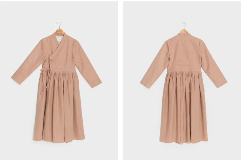 Puede incluir: Un vestido largo de color rosa claro con mangas largas, cuello de envoltura y falda fruncida.