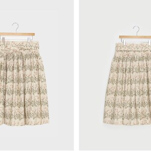 Puede incluir: Una falda midi de color crema con estampado floral de peque&ntilde;as hojas verdes y flores rosas. La falda tiene una cintura fruncida y un lazo en la parte delantera.