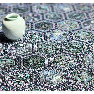 Może przedstawiać: Mały, jasnozielony ceramiczny wazon o gładkim, zaokrąglonym kształcie stoi na czarno-białej powierzchni z wzorem. Powierzchnia wykonana jest z małych, opalizujących płytek ułożonych w sześciokątny wz&oacute;r.