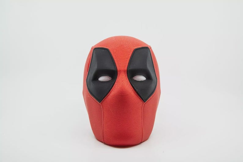 May include: A red Deadpool mask with black eye and mouth details. The mask has a textured surface and is set against a white background. The eye openings have a mesh material.