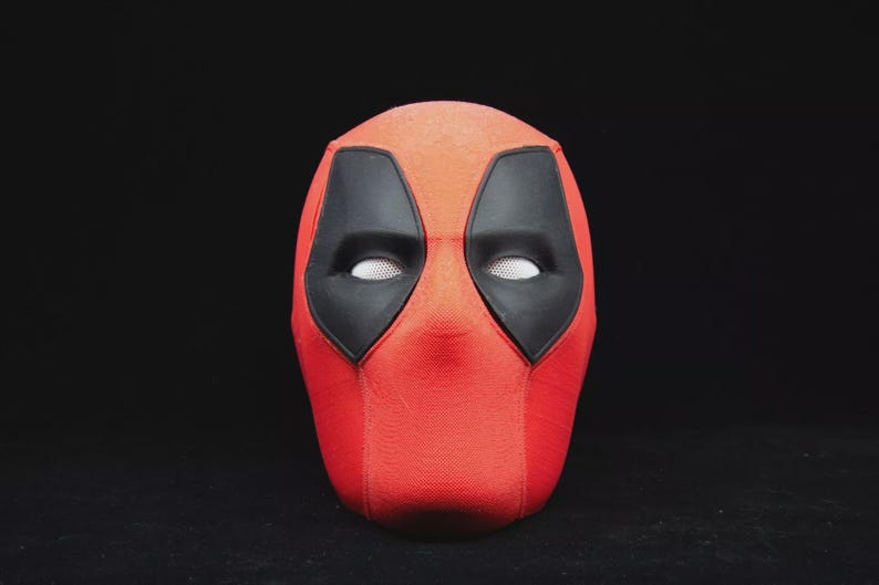 May include: A red Deadpool mask with black eye coverings and white mesh eye openings. The mask is a full head covering, with a textured surface. The mask is a costume accessory.