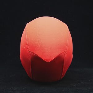 May include: A red, fabric-covered object with a rounded top and a pointed, V-shaped bottom. The object is set against a black background, with the color gradient shifting from a darker red at the base to a lighter shade at the top.