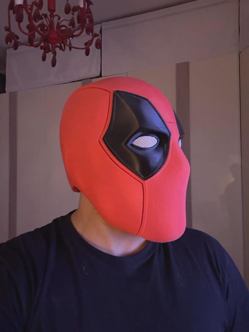 May include: A red Deadpool mask with black eye coverings and a white mesh eye area. The mask is a full head covering, and the design is based on the comic book character. The mask is made of a smooth material.