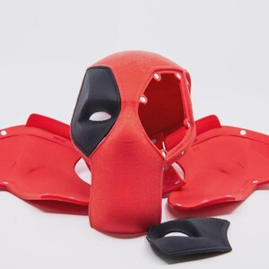 May include: A red and black Deadpool mask with matching red ear pieces and a separate black eye mask. The mask has a mesh eye covering and is made of a textured material. The ear pieces have white button-like details.