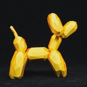 Puede incluir: Escultura de perro globo geométrico amarillo. El perro está hecho de formas angulares conectadas, lo que le da una apariencia facetada. La escultura está sobre un fondo negro.