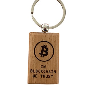 Könnte beinhalten: Ein Holzschlüsselanhänger mit einem silbernen Schlüsselring. Der Schlüsselanhänger hat ein kreisförmiges Design mit einem Bitcoin-Symbol und dem Text "IN BLOCKCHAIN WE TRUST".