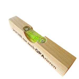 May include: A wooden level with the text "jetzt hilft nur noch OPA rieren" engraved on it. The level has a green bubble in the center.