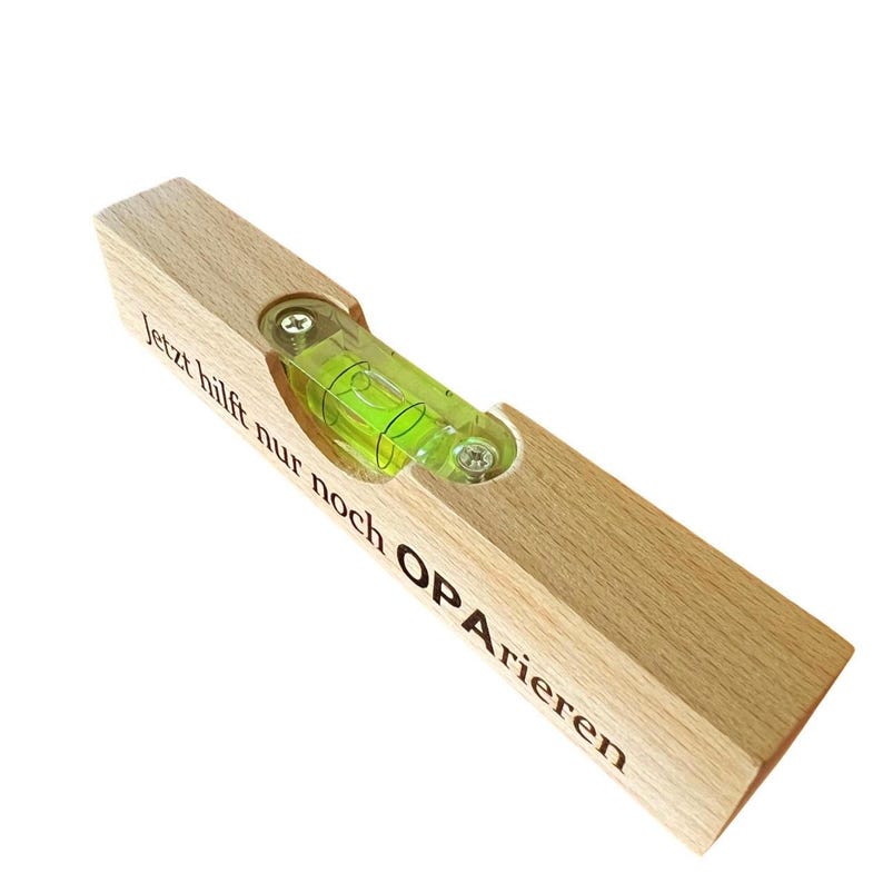 May include: A wooden level with the text "jetzt hilft nur noch OPA rieren" engraved on it. The level has a green bubble in the center.