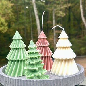 May include: Four Christmas tree shaped candles on a gray tray. The candles are green, red, and white.