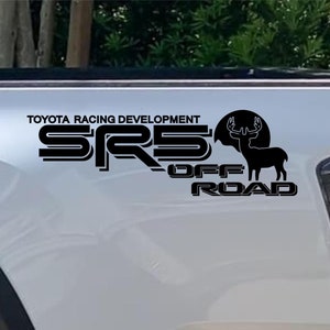 May include: Black decal featuring the text "TOYOTA RACING DEVELOPMENT SRS OFF ROAD" and a silhouette of a deer with antlers. The decal is applied to the white body of a truck.
