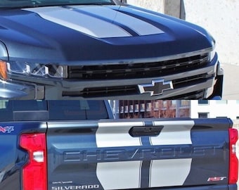 May include: A dark blue Chevrolet Silverado pickup truck with a 4x4 emblem on the side and a silver and black racing stripe decal on the hood and tailgate. The truck has a black bumper and a black tow hitch.