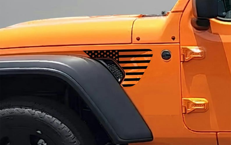 May include: Orange vehicle with a black and orange American flag graphic on the side panel. The flag design features black stripes and stars, adding a patriotic touch to the car's exterior. The vehicle's tire and fender are also visible.