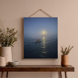 Peut inclure: Une impression encadrée d'un paysage marin serein au crépuscule. Deux personnes sont sur un petit bateau dans l'eau, avec une lune ou un soleil brillant se reflétant sur l'eau. Le ciel est un dégradé de bleu.