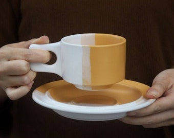 May include: A white and yellow ceramic teacup and saucer set. The cup has a white interior and a yellow exterior. The saucer is yellow on the inside and white on the outside.