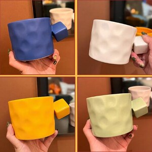May include: Four ceramic mugs with a textured surface and a square handle. The mugs are in different colors: blue, white, yellow, and green.