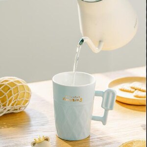 May include: A light blue ceramic mug with a popsicle-shaped handle. The mug has a textured design and the words "everyday amazing" written in gold lettering. The mug is being filled with water from a white teapot.