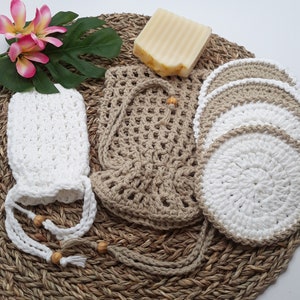 May include: A set of zero waste bathroom essentials, including a crocheted soap sack, a set of reusable cotton rounds, and a bar of soap. The items are arranged on a woven straw mat.