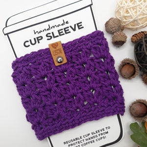 Black currant color cozy displayed over a white paper coffee sleeve insert card in the shape of a take out cup and lid. On top the words handmade Cup Sleeve. Shows how sharp the cozy would look over a take out cup from a coffee shop or restaurant.