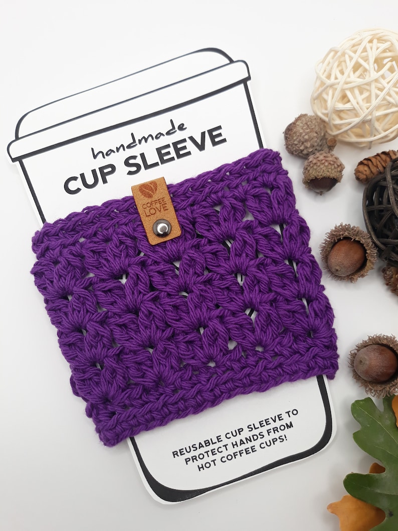 Black currant color cozy displayed over a white paper coffee sleeve insert card in the shape of a take out cup and lid. On top the words handmade Cup Sleeve. Shows how sharp the cozy would look over a take out cup from a coffee shop or restaurant.