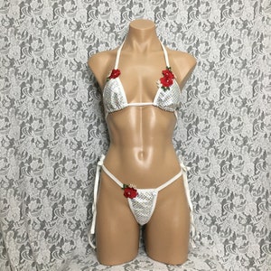 May include: White sequined bikini with red flower embellishments. The top is a triangle style and the bottom is a cheeky cut.