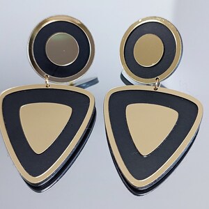 May include: A pair of black and gold geometric earrings. The earrings are made of two pieces: a round disc with a smaller gold circle in the center, and a triangle with a gold triangle in the center.