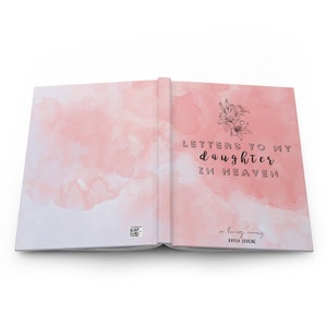 May include: An open book with a pink watercolor background. The cover reads "Letters to my daughter in heaven" with a floral design. The inside cover reads "in loving memory" with the name "Kayla Lovene".