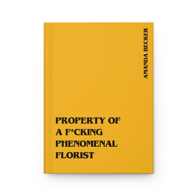 May include: A bright yellow hardcover journal featuring bold black text that reads PROPERTY OF A F*CKING PHENOMENAL FLORIST on the front cover, with the name AMANDA BECKER printed vertically in black along the right side of the cover.