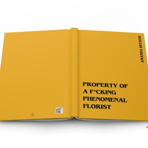 May include: A mustard yellow hardcover book laid open flat. The front cover features the black text PROPERTY OF A F*CKING PHENOMENAL FLORIST and the author name AMANDA BECKER. A small square barcode and a tiny logo are visible on the back cover.