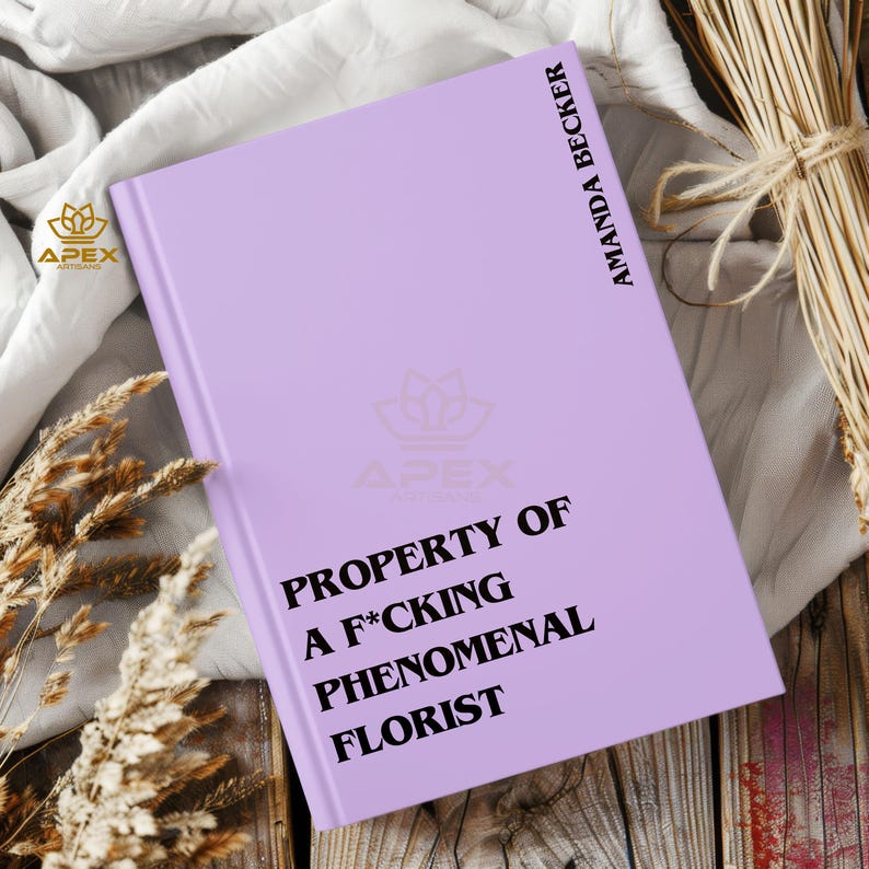 May include: A light purple hardcover book with black text on the front cover that reads PROPERTY OF A F*CKING PHENOMENAL FLORIST and the author name AMANDA BECKER printed vertically along the right edge of the cover in black capital letters.