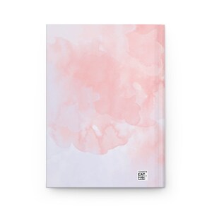 May include: A softcover notebook with a pink watercolor design on the cover. The design features light pink and white watercolor washes that blend together.