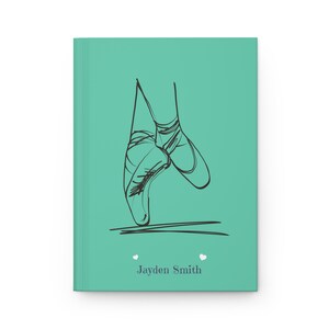 May include: A teal hardcover journal featuring a black line art illustration of ballet pointe shoes on the front cover. Below the illustration, the name Jayden Smith is printed in a dark gray serif font, flanked by two small white heart icons.