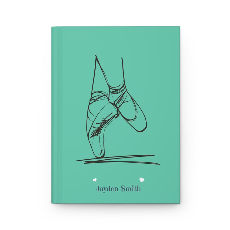 May include: A teal hardcover journal featuring a black line art illustration of ballet pointe shoes on the front cover. Below the illustration, the name Jayden Smith is printed in a dark gray serif font, flanked by two small white heart icons.