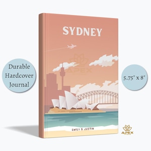 Może przedstawiać: Różowy notes w twardej oprawie z kolorową ilustracją Opery w Sydney i mostu Harbour Bridge. Notes ma wymiary 5,75 cala na 8 cali i napis "Sydney" na okładce. Tekst "Emily & Justin" jest nadrukowany na dole okładki.