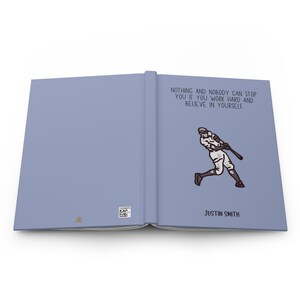 May include: A light blue journal with the text "NOTHING AND NOBODY CAN STOP YOU IF YOU WORK HARD AND BELIEVE IN YOURSELF." and an illustration of a baseball player swinging a bat. The journal is labeled "JUSTIN SMITH".