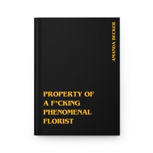 May include: A black hardcover journal featuring bold yellow text on the front cover that reads PROPERTY OF A F*CKING PHENOMENAL FLORIST. The name AMANDA BECKER is printed vertically in yellow text along the right side of the front cover.