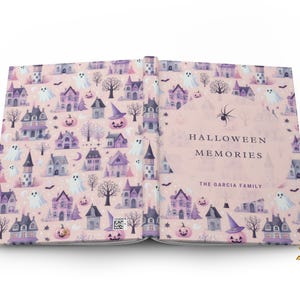 May include: A pink and purple scrapbook with a Halloween theme. The cover features a pattern of houses, ghosts, pumpkins, and bats. The title "Halloween Memories" is printed on the cover, along with the text "The Garcia Family".