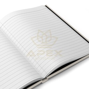 May include: An open notebook with white lined pages. The centre of the pages features a light tan logo of a stylised lotus flower above the text APEX ARTISANS. The notebook has a light-coloured cover and a black spine visible at the binding.