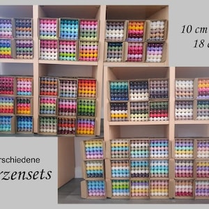 Könnte beinhalten: Sortiment an bunten Kerzensets in verschiedenen Größen, auf Regalen ausgestellt. Die Sets beinhalten 10 cm oder 18 cm Kerzen. Der Text "verschiedene Kerzensets" ist unten links sichtbar.