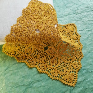 May include: Mustard yellow crocheted doilies with intricate floral patterns. The handmade lace pieces are displayed on a white surface and a green textured background. The doilies have a scalloped edge and a delicate, openwork design.