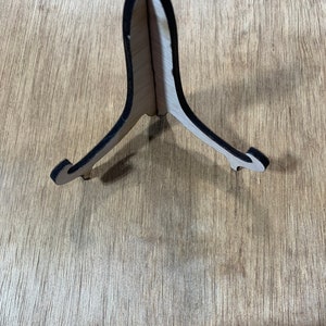 May include: A wooden easel stand with a black painted edge. The stand is made of light wood and has a triangular shape.