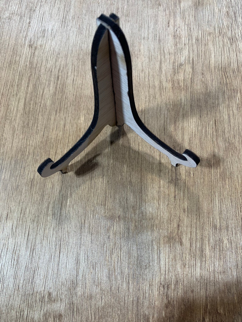 May include: A wooden easel stand with a black painted edge. The stand is made of light wood and has a triangular shape.
