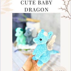 May include: A light blue crocheted baby dragon with white horns and wings. The dragon is held in a hand, with two other dragons in the background. The text "CROCHET PATTERN" and "CUTE BABY DRAGON" are at the top of the image.