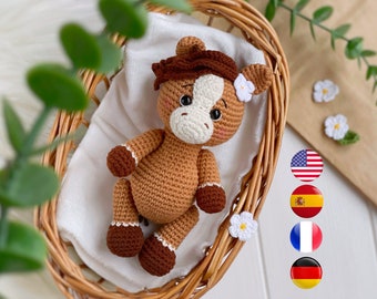 May include: A brown and tan crocheted horse toy with a white muzzle, dark brown mane, and dark brown hooves. The horse features black safety eyes, pink blush on the cheeks, and a small white crocheted flower attached to one ear.