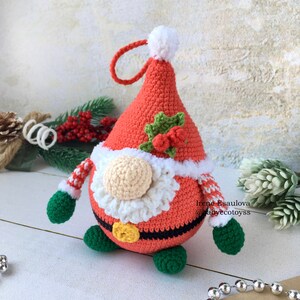 Pu&ograve; includere: Ornamento natalizio a forma di gnomo fatto a mano all'uncinetto. Lo gnomo indossa un cappello rosso con pompon e finiture bianche, una barba color crema e una cintura nera con fibbia dorata. Braccia a righe verdi e bianche e piedi verdi completano il look festivo.