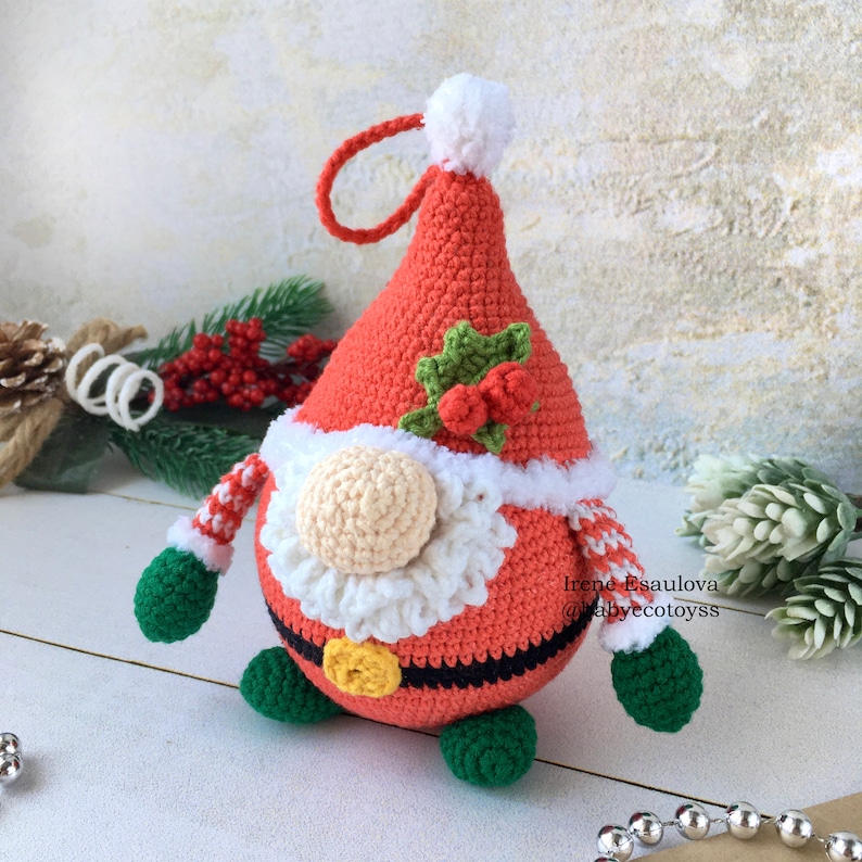 Pu&ograve; includere: Ornamento natalizio a forma di gnomo fatto a mano all'uncinetto. Lo gnomo indossa un cappello rosso con pompon e finiture bianche, una barba color crema e una cintura nera con fibbia dorata. Braccia a righe verdi e bianche e piedi verdi completano il look festivo.